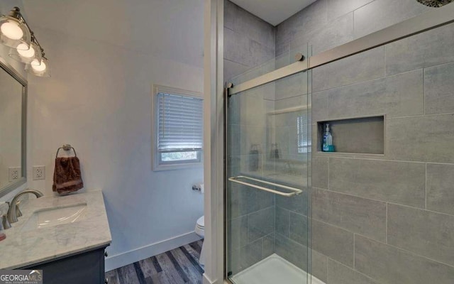 bathroom with toilet, wood finished floors, a shower stall, baseboards, and vanity