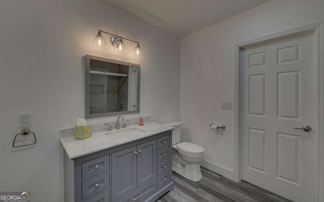 bathroom with toilet, wood finished floors, tiled shower, baseboards, and vanity