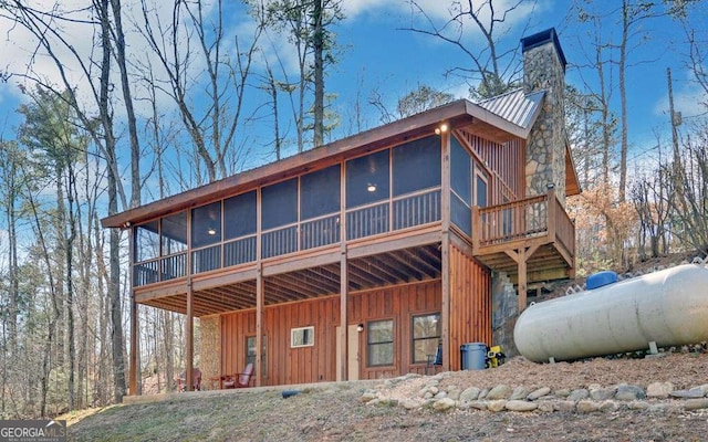 exterior space featuring a chimney, board and batten siding, metal roof, and a sunroom