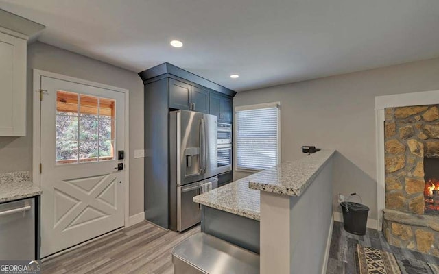 kitchen with light stone countertops, light wood finished floors, a peninsula, recessed lighting, and appliances with stainless steel finishes