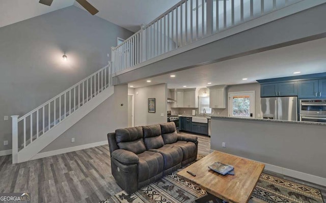 living room featuring baseboards, stairway, recessed lighting, a towering ceiling, and wood finished floors