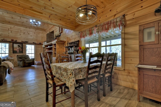dining area featuring high vaulted ceiling, wooden ceiling, a notable chandelier, wooden walls, and light wood-type flooring