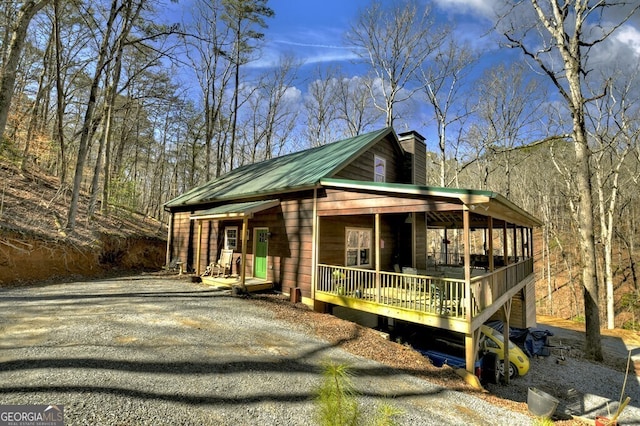 view of property exterior featuring covered porch, metal roof, a chimney, and gravel driveway