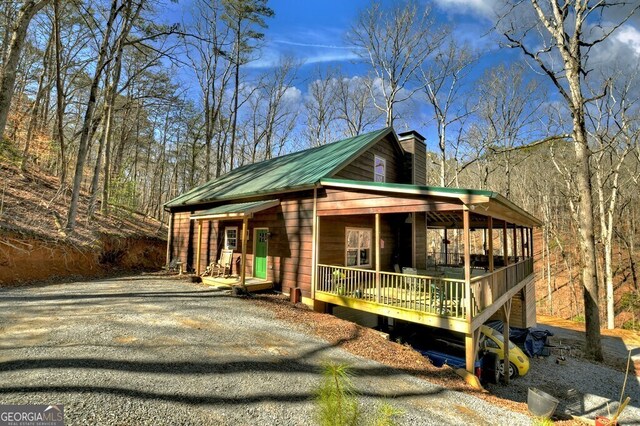 view of front of home featuring metal roof, covered porch, driveway, and a chimney