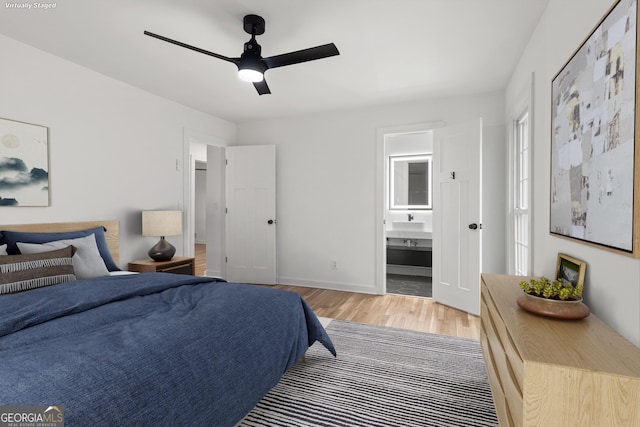 bedroom featuring ensuite bathroom, baseboards, light wood-style flooring, and a ceiling fan