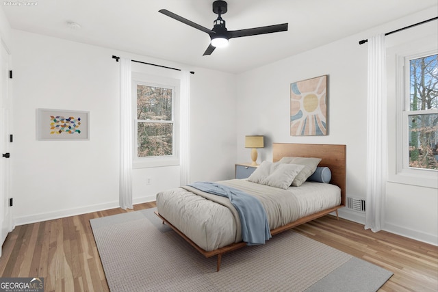 bedroom featuring a ceiling fan, wood finished floors, visible vents, and baseboards