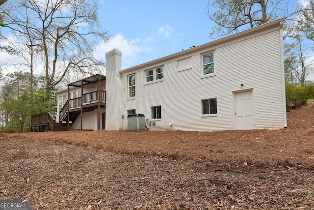 back of house featuring a chimney, brick siding, a deck, and stairs