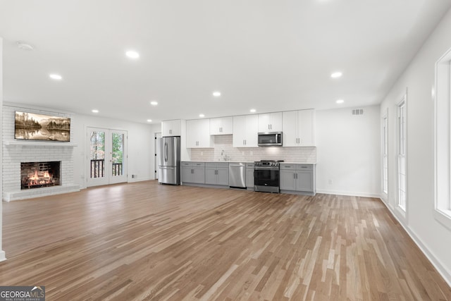 unfurnished living room with a brick fireplace, a sink, visible vents, and light wood-style floors