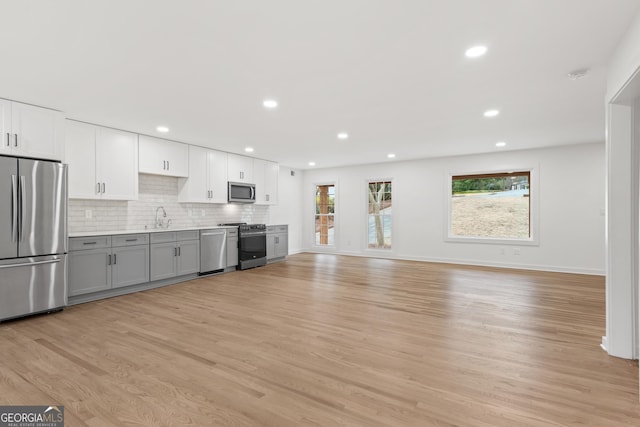 kitchen featuring light wood finished floors, stainless steel appliances, tasteful backsplash, gray cabinets, and a sink