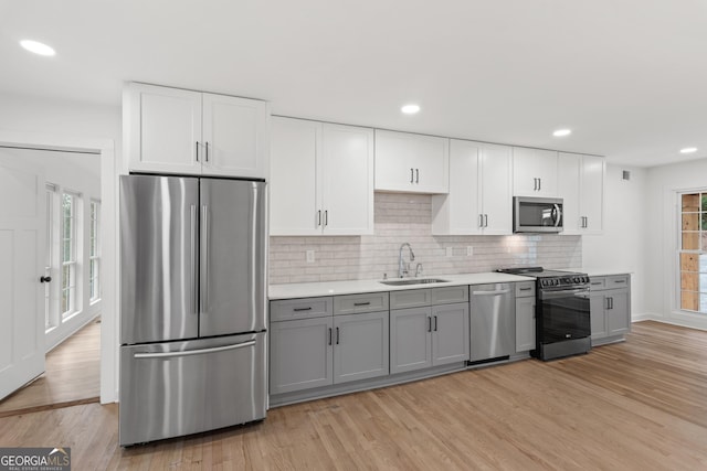 kitchen with appliances with stainless steel finishes, gray cabinets, a sink, and light wood finished floors