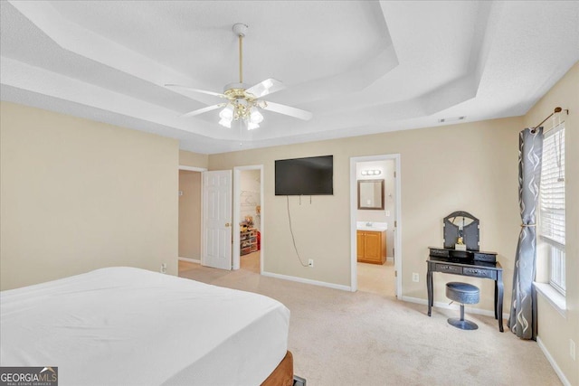 bedroom featuring light carpet, visible vents, baseboards, a raised ceiling, and ensuite bath