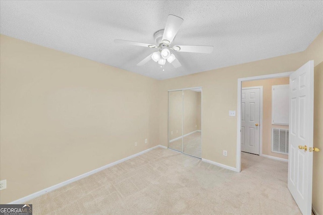 unfurnished bedroom featuring light carpet, baseboards, visible vents, a textured ceiling, and a closet