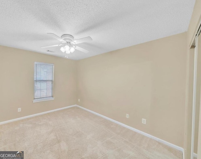 empty room with light colored carpet, visible vents, a ceiling fan, a textured ceiling, and baseboards