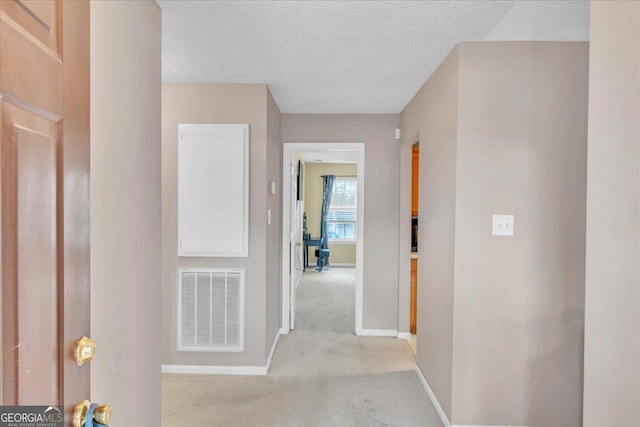 hallway with carpet floors, baseboards, visible vents, and a textured ceiling