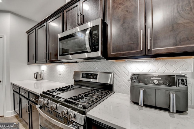 kitchen with backsplash, stainless steel appliances, light stone countertops, and dark brown cabinets