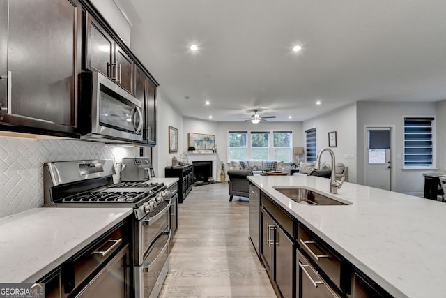 kitchen with a sink, backsplash, open floor plan, stainless steel appliances, and a fireplace