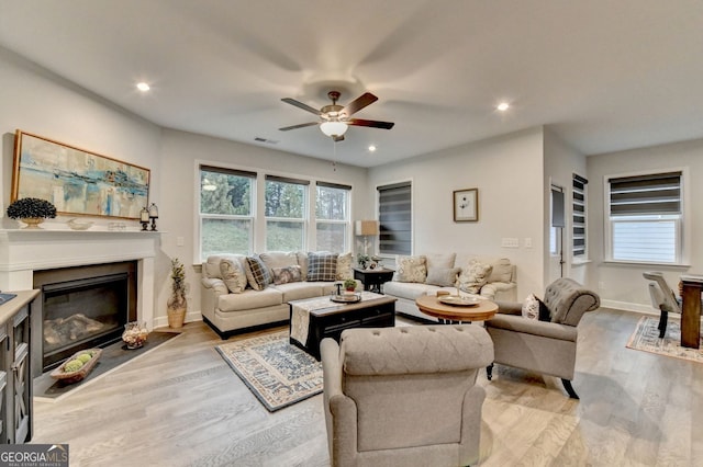 living area featuring light wood-type flooring, visible vents, plenty of natural light, and a glass covered fireplace