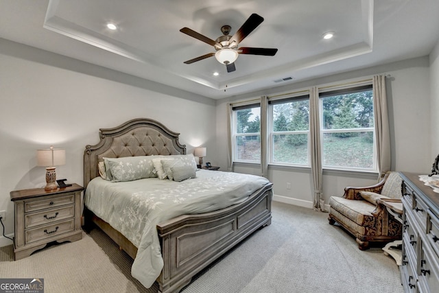 bedroom with a tray ceiling, light colored carpet, visible vents, and baseboards