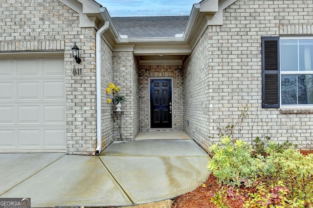 view of exterior entry with brick siding, an attached garage, and roof with shingles