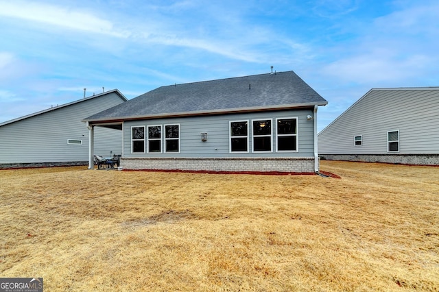 rear view of house with a yard, brick siding, and roof with shingles