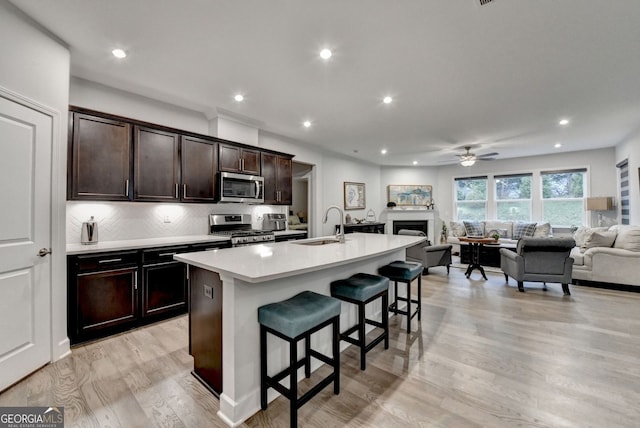 kitchen featuring open floor plan, an island with sink, light countertops, a kitchen breakfast bar, and stainless steel appliances