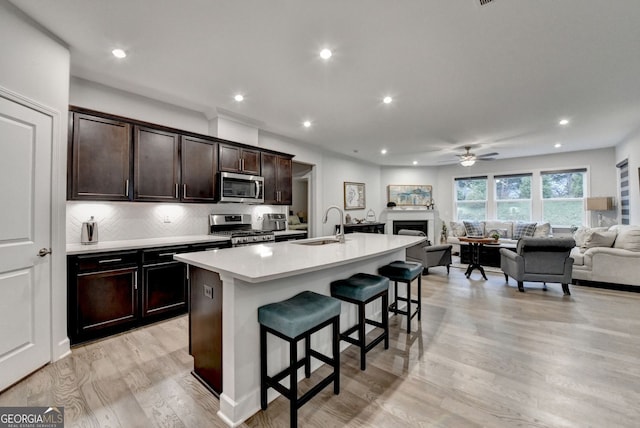 kitchen with a ceiling fan, a center island with sink, open floor plan, a breakfast bar, and stainless steel appliances