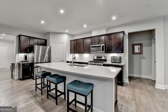 kitchen featuring appliances with stainless steel finishes, a sink, light wood-style floors, a breakfast bar area, and decorative backsplash