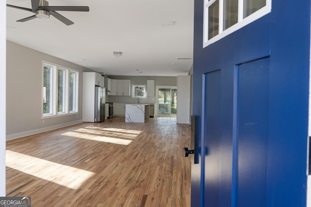 unfurnished living room featuring light wood-style floors, a ceiling fan, baseboards, and a wealth of natural light