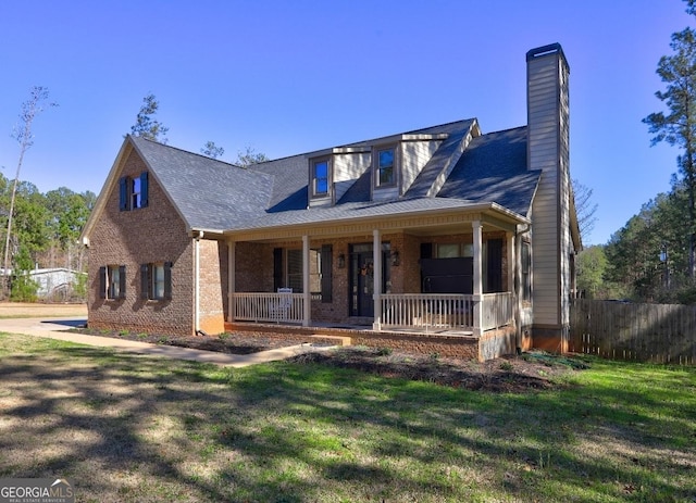 view of front of property with covered porch, brick siding, fence, a front lawn, and a chimney