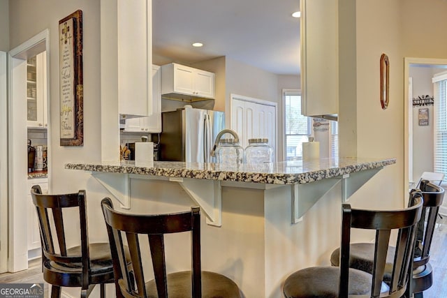 kitchen featuring light stone counters, freestanding refrigerator, white cabinetry, a sink, and a peninsula