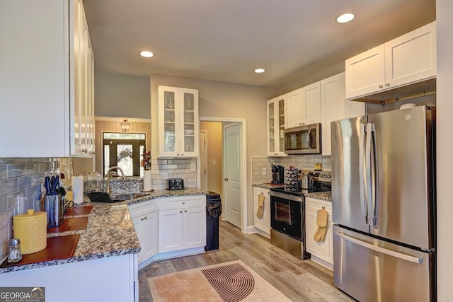 kitchen with stainless steel appliances, a sink, white cabinets, light wood-type flooring, and dark stone counters