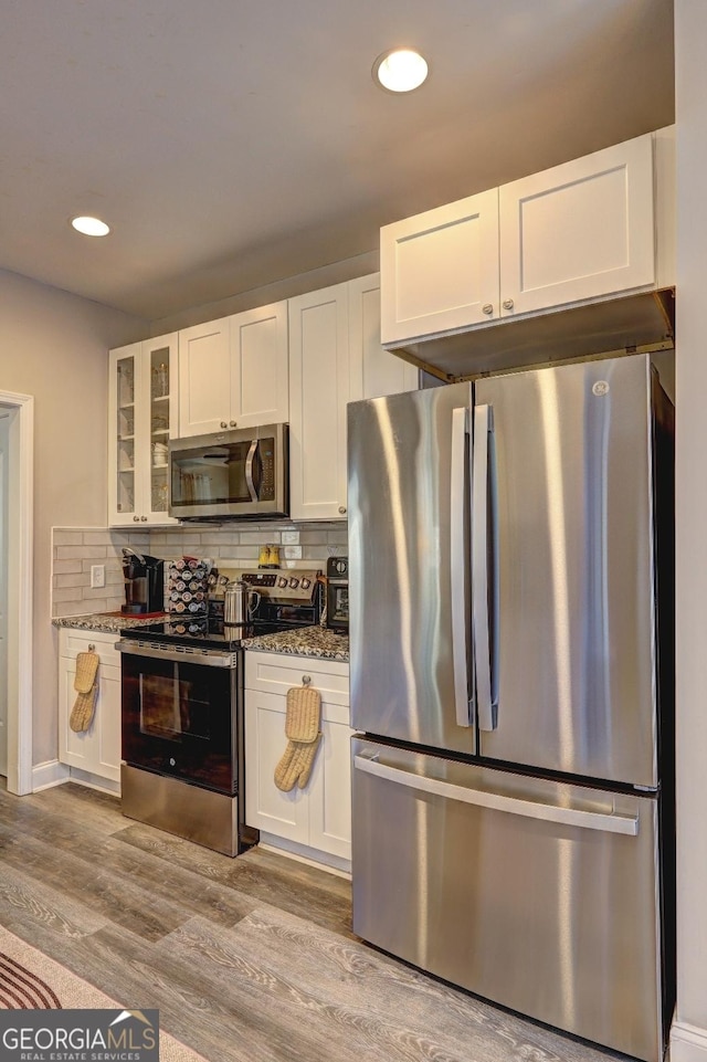 kitchen featuring decorative backsplash, glass insert cabinets, appliances with stainless steel finishes, wood finished floors, and white cabinetry