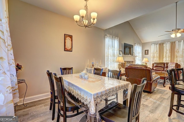 dining space with a fireplace, light wood finished floors, lofted ceiling, baseboards, and ceiling fan with notable chandelier