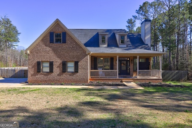 view of front of property featuring a chimney, covered porch, fence, a front lawn, and brick siding