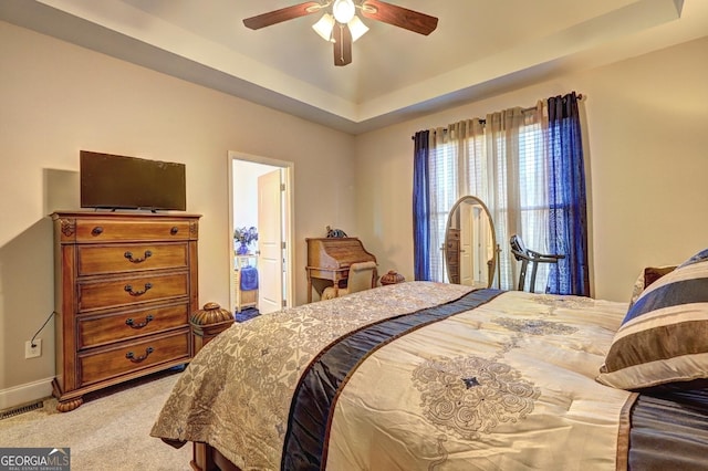 bedroom featuring light carpet, visible vents, ceiling fan, ensuite bathroom, and a tray ceiling