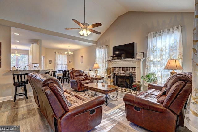 living room featuring ceiling fan with notable chandelier, lofted ceiling, a brick fireplace, and wood finished floors