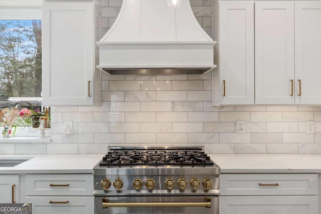 kitchen featuring tasteful backsplash, high end stainless steel range oven, light countertops, and custom range hood