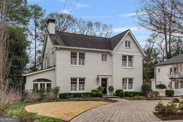 view of front of home with brick siding, a chimney, and fence