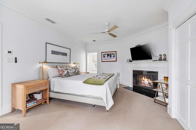 bedroom featuring a ceiling fan, visible vents, a fireplace with flush hearth, ornamental molding, and light colored carpet