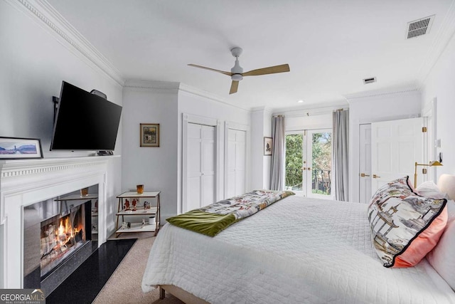 carpeted bedroom with visible vents, a warm lit fireplace, crown molding, access to outside, and two closets