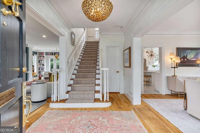 foyer entrance with ornamental molding, wood finished floors, an inviting chandelier, wainscoting, and stairs