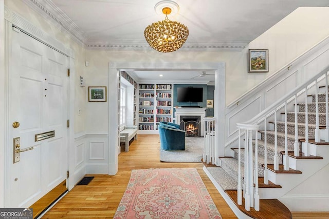 entrance foyer with stairway, crown molding, a decorative wall, and wood finished floors