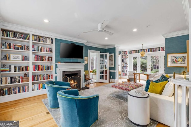 living area featuring wood finished floors, a fireplace with flush hearth, ceiling fan, ornamental molding, and french doors