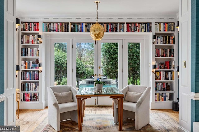 sitting room with light wood finished floors, french doors, bookshelves, and ornamental molding