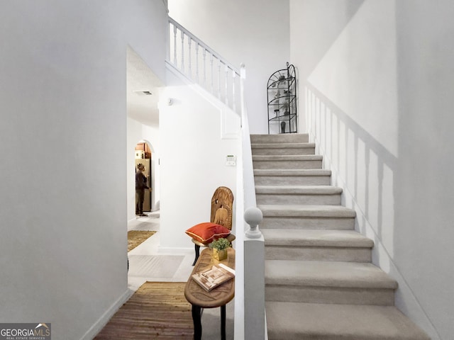 stairs featuring a towering ceiling and wood finished floors