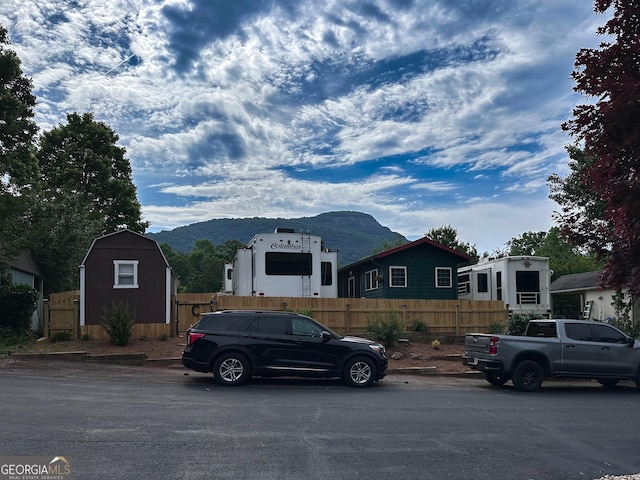 view of front facade featuring an outbuilding, a mountain view, a storage shed, and fence