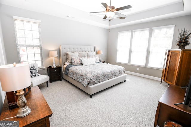 bedroom featuring a tray ceiling, light carpet, baseboards, and multiple windows