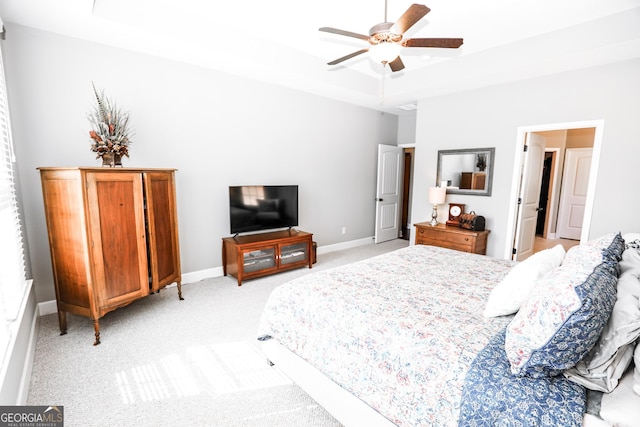 bedroom with a ceiling fan, a raised ceiling, light colored carpet, and baseboards