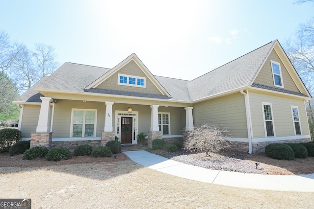 craftsman house featuring stone siding, covered porch, and roof with shingles