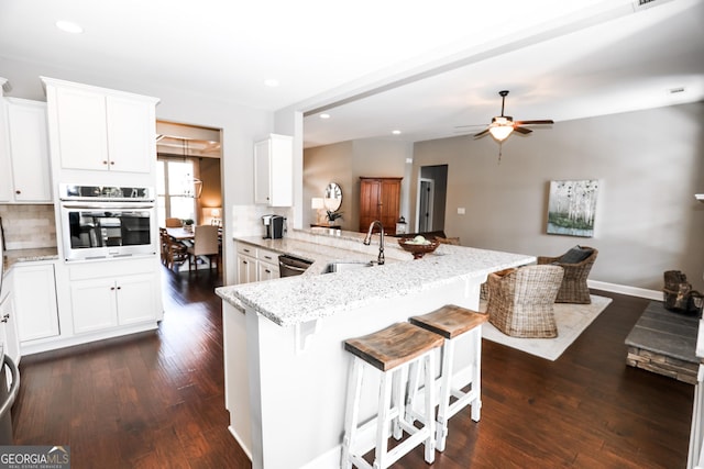 kitchen featuring a breakfast bar, dark wood finished floors, stainless steel appliances, a sink, and light stone countertops